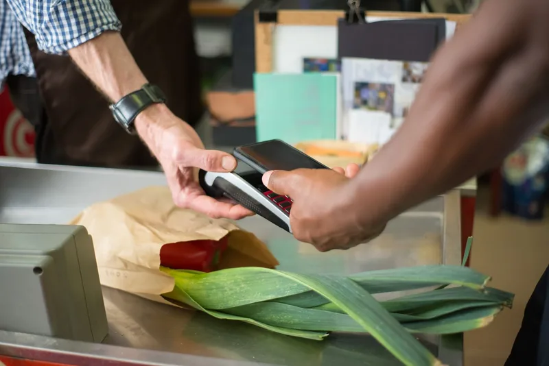 Cashier and customer at a shop counter using a handheld card payment terminal