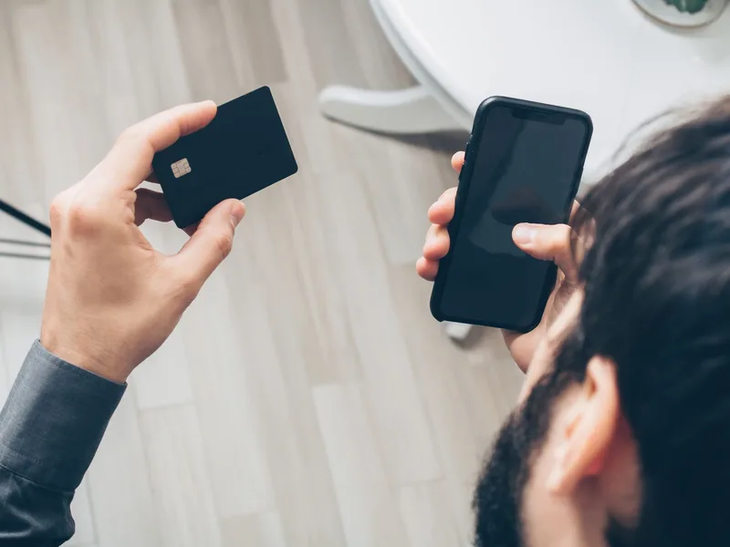 Man holding a bank card in one hand and a smartphone in the other, about to confirm an online payment